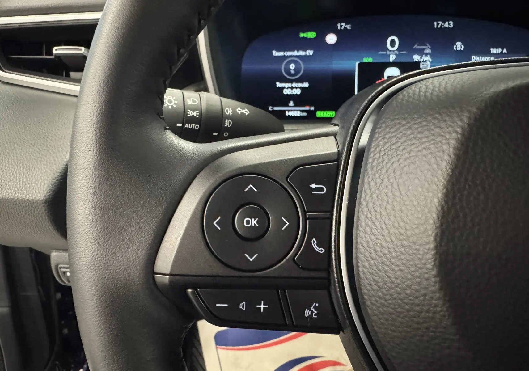 Gros plan sur le volant côté gauche du Suzuki Swace 2025, avec commandes multifonctions et tableau de bord numérique en arrière-plan.