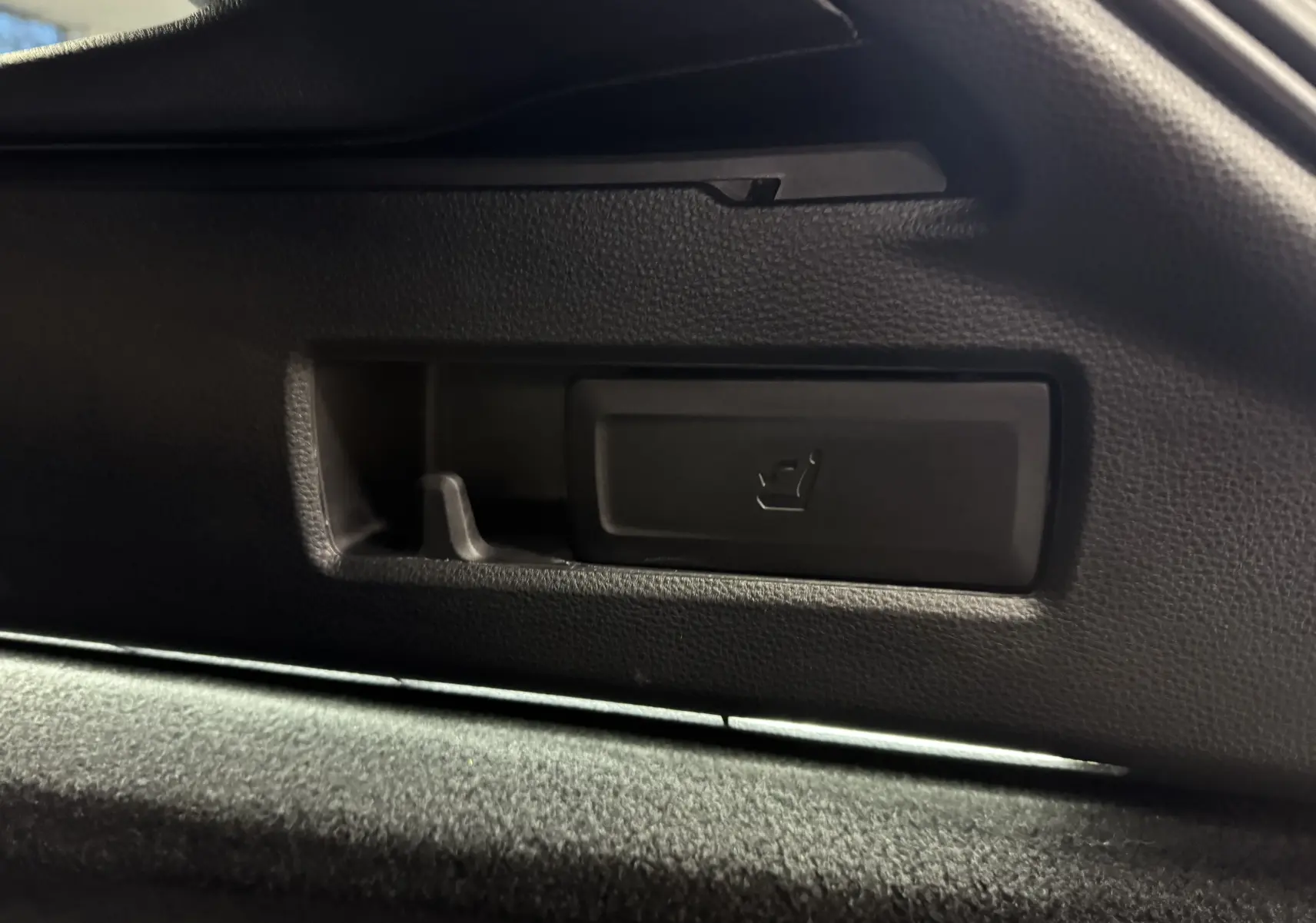 Détail intérieur montrant le bouton de réglage de siège en plastique noir sur la portière d'une Suzuki Swace bleue 2025.