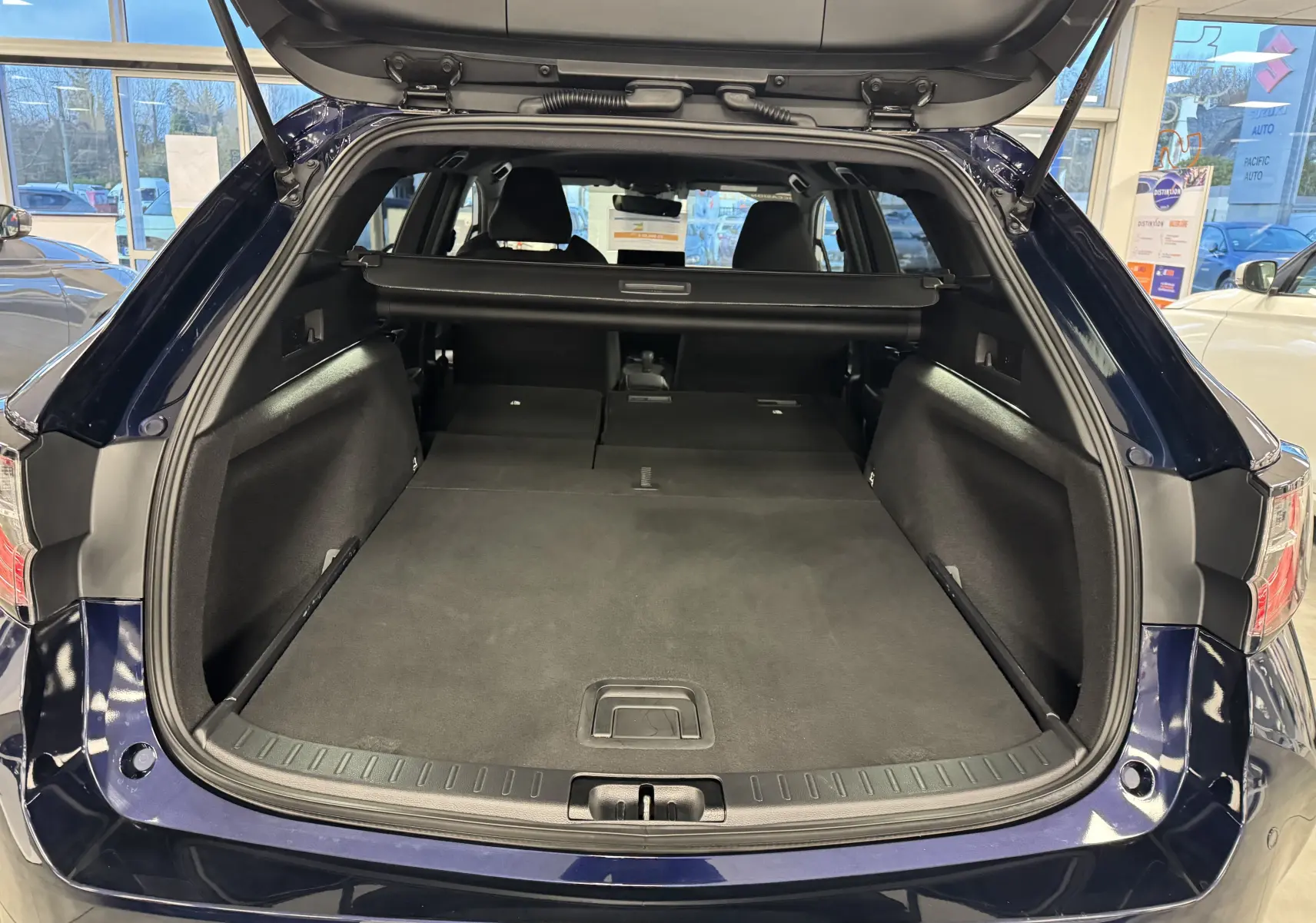 Coffre ouvert en vue arrière d’une Suzuki Swace 2025 bleu, montrant l’espace de chargement plat et la plage arrière rétractable.