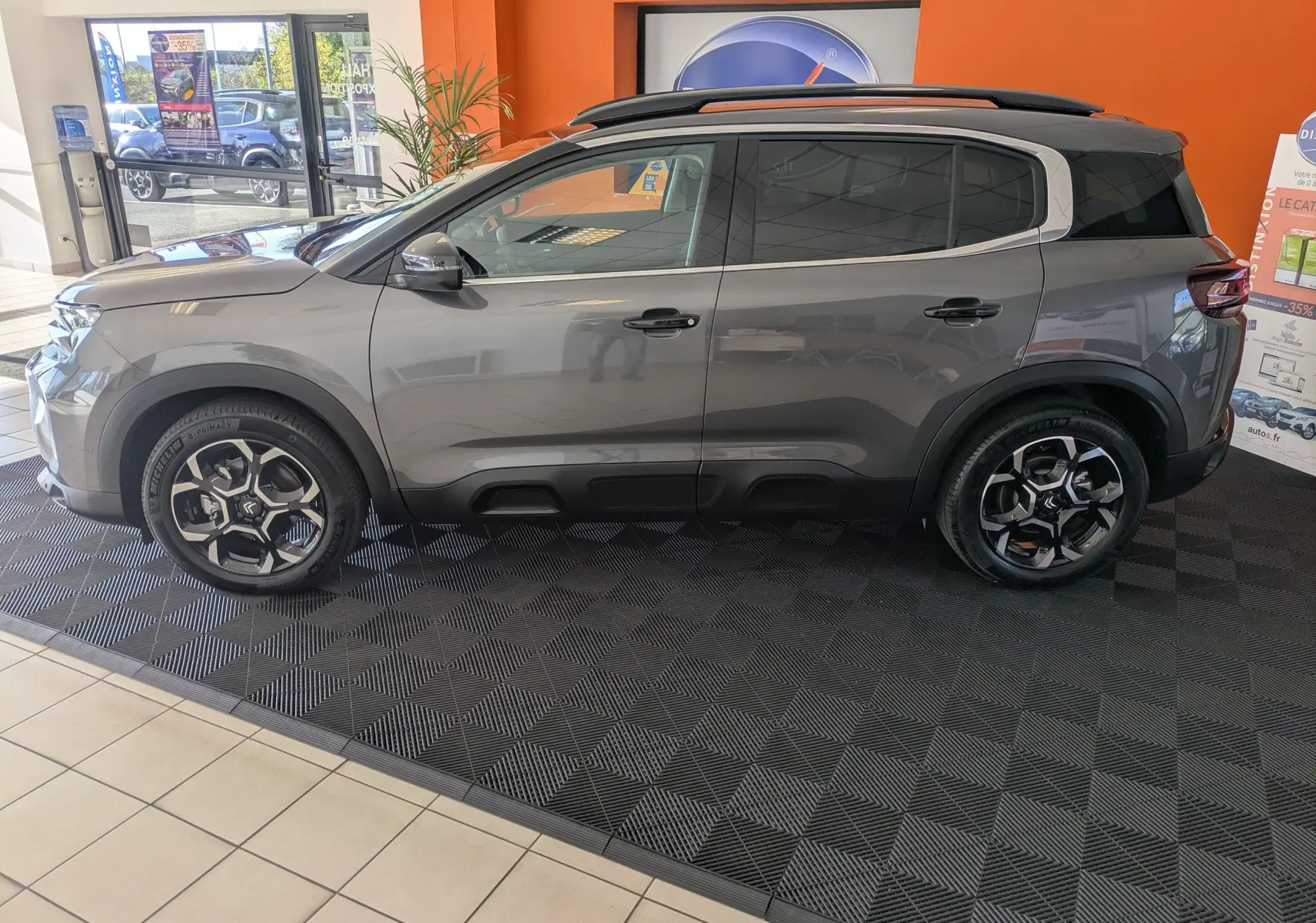 Vue de profil côté gauche d'un Citroën C5 Aircross hybride gris platinium avec jantes biton 18 pouces en showroom.