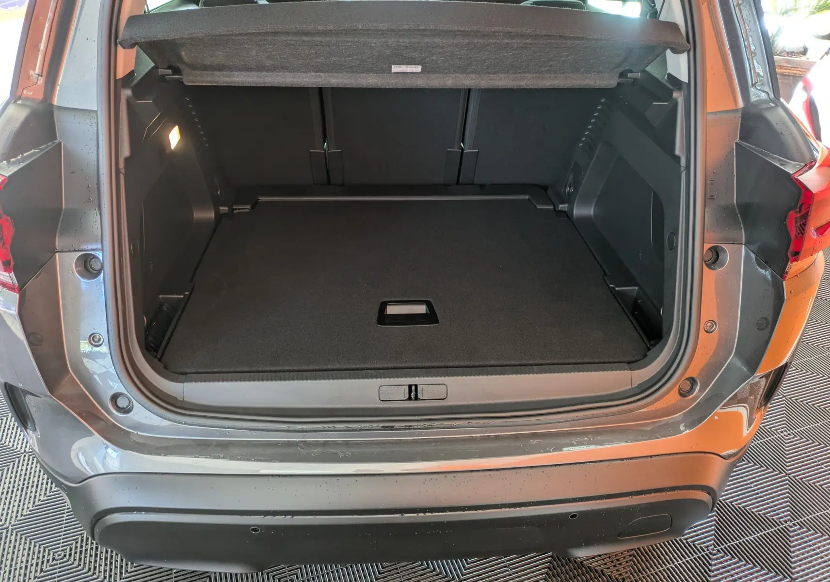 Coffre ouvert vu de l'arrière d'un Citroën C5 Aircross hybride gris platinium avec intérieur noir et éclairage latéral.