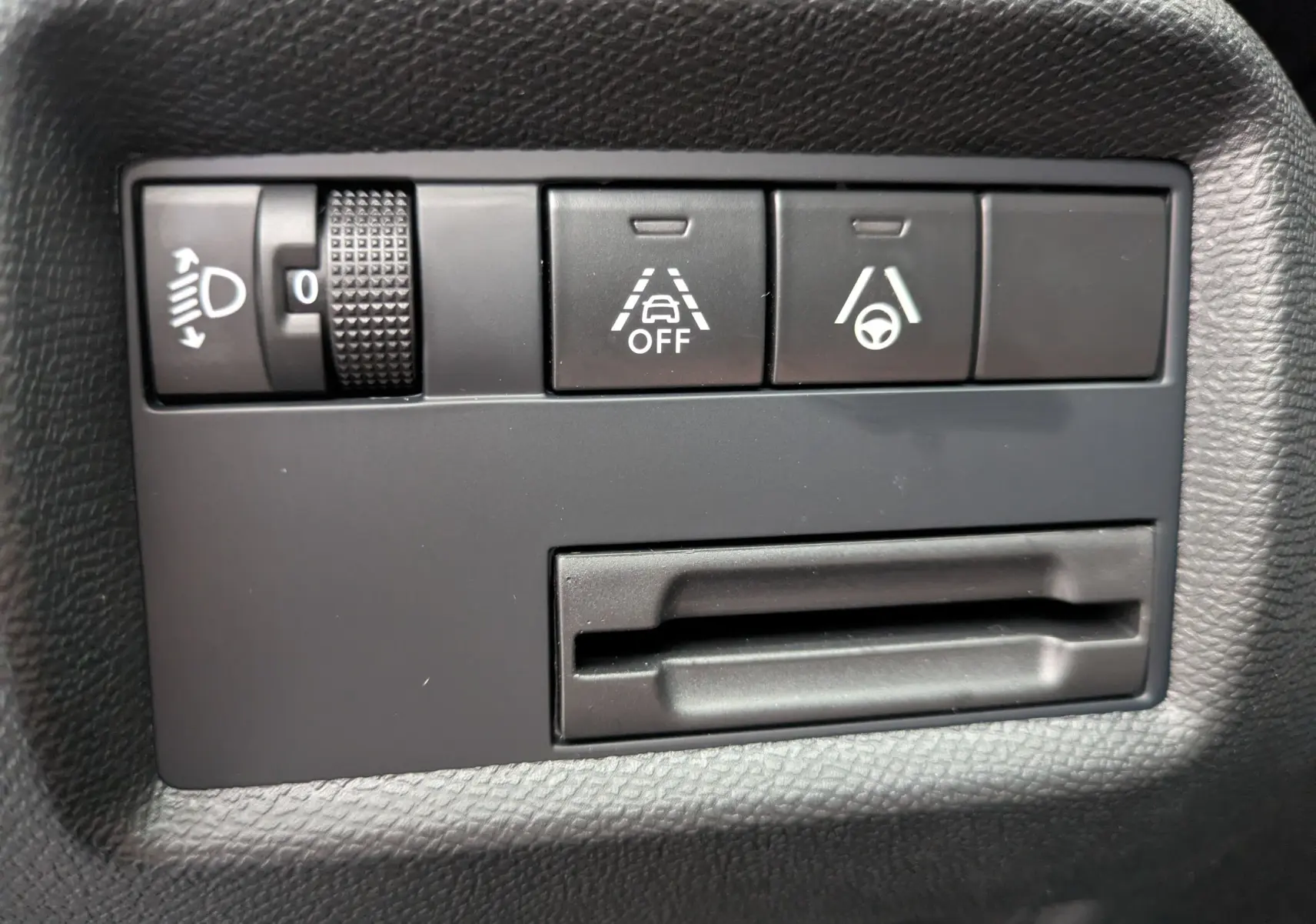Gros plan sur les commandes de réglage des phares et d’aide à la conduite dans un Citroën C5 Aircross hybride gris platinium.