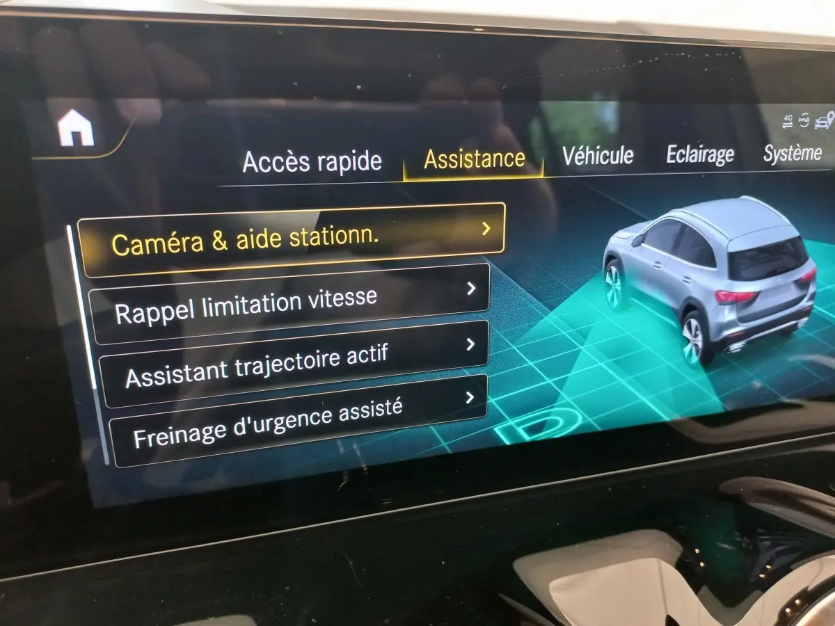 Écran tactile intérieur montrant l'assistance au stationnement avec vue 3/4 arrière d'un Mercedes GLA gris foncé.