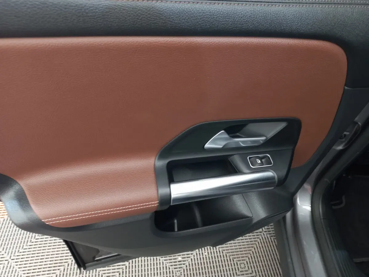 Gros plan sur la porte intérieure côté droit du Mercedes GLA gris foncé, avec garniture cuir marron et poignée argentée.
