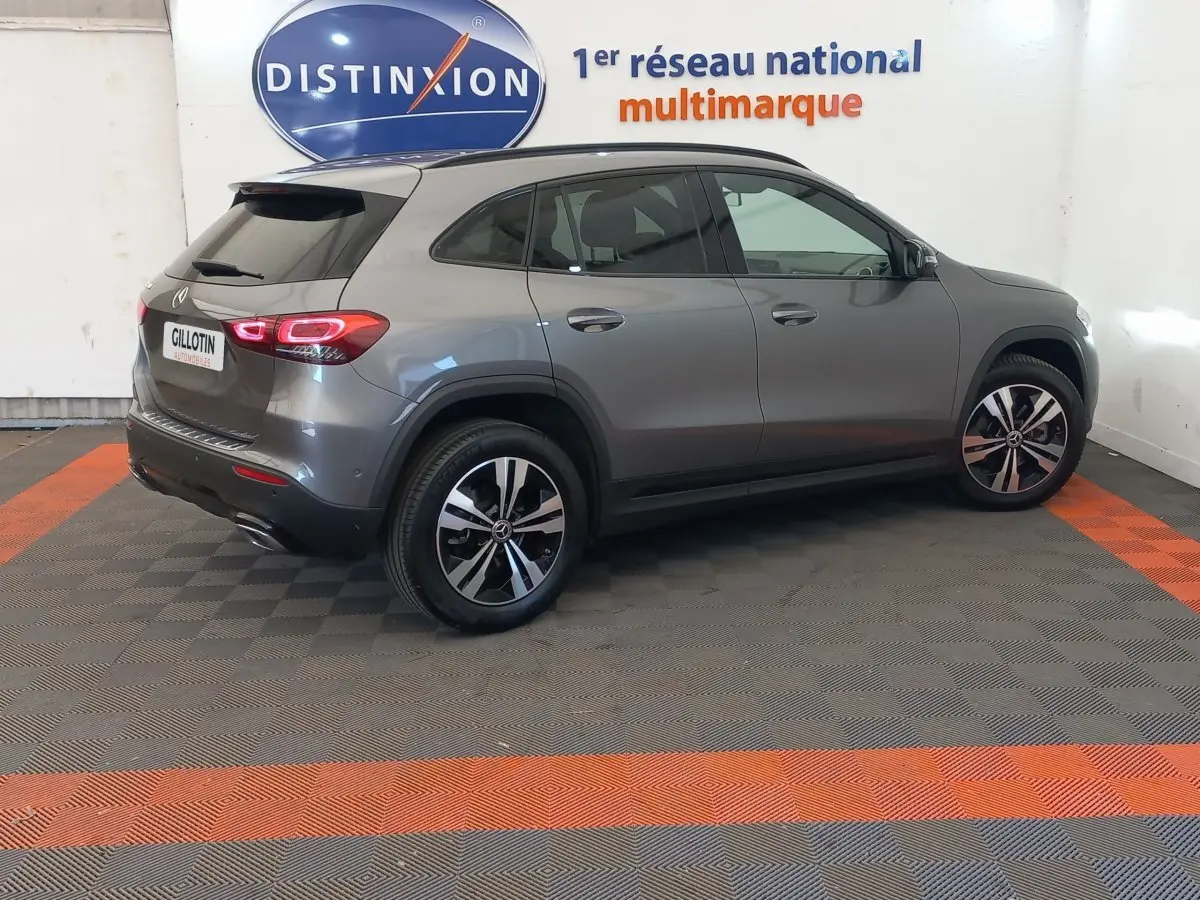 Vue 3/4 arrière droite d’un Mercedes GLA 200 Business Line gris foncé avec jantes alliage et feux LED allumés en intérieur showroom.