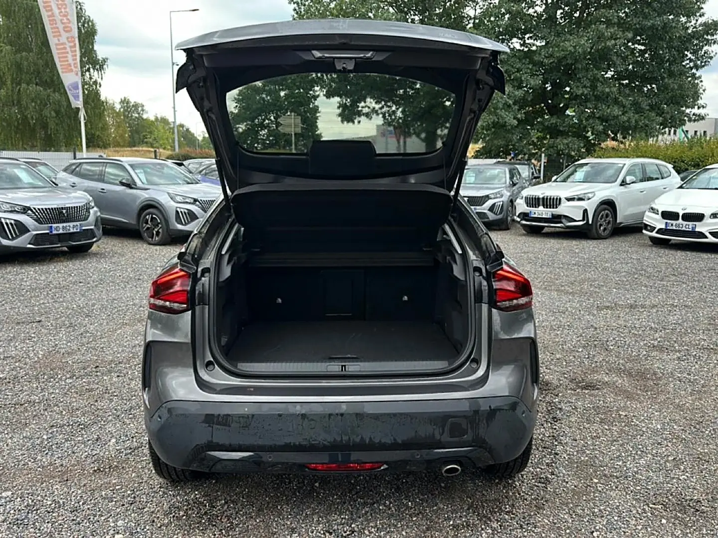 Vue arrière d'une Citroën C4 gris 2024 avec coffre ouvert sur un parking extérieur.
