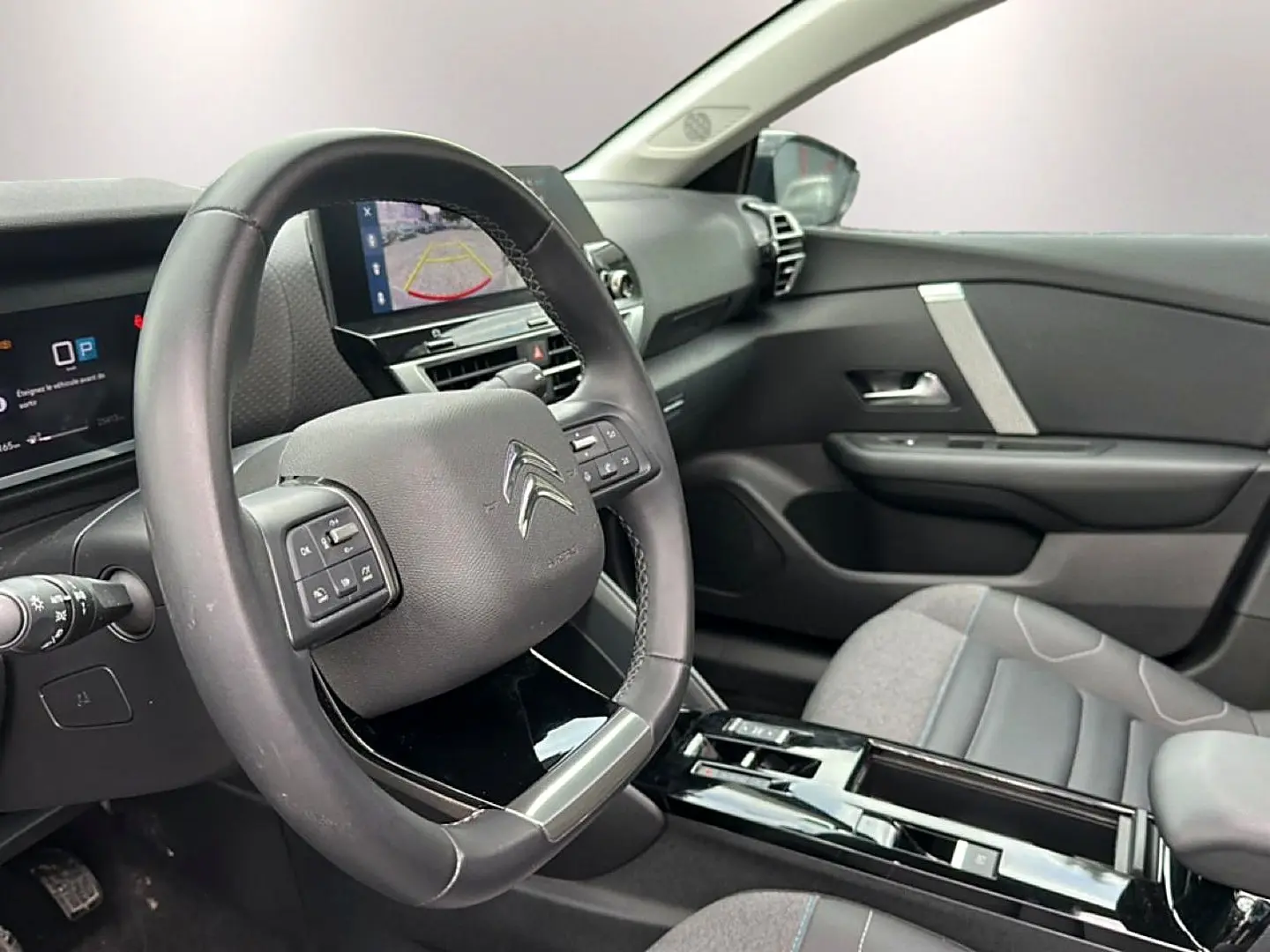 Vue intérieure côté conducteur de la Citroën C4 2024, volant cuir noir et écran tactile affichant la caméra de recul.