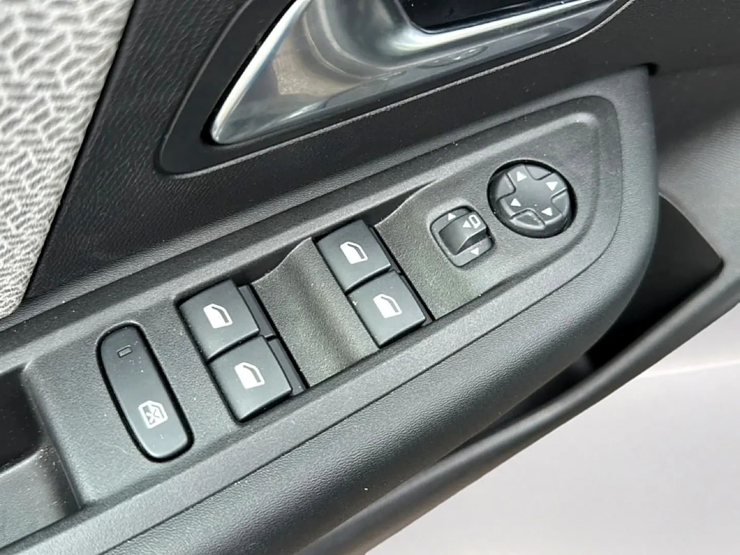 Gros plan sur les commandes de lève-vitres et réglages des rétroviseurs côté gauche d'une Citroën C4 gris.
