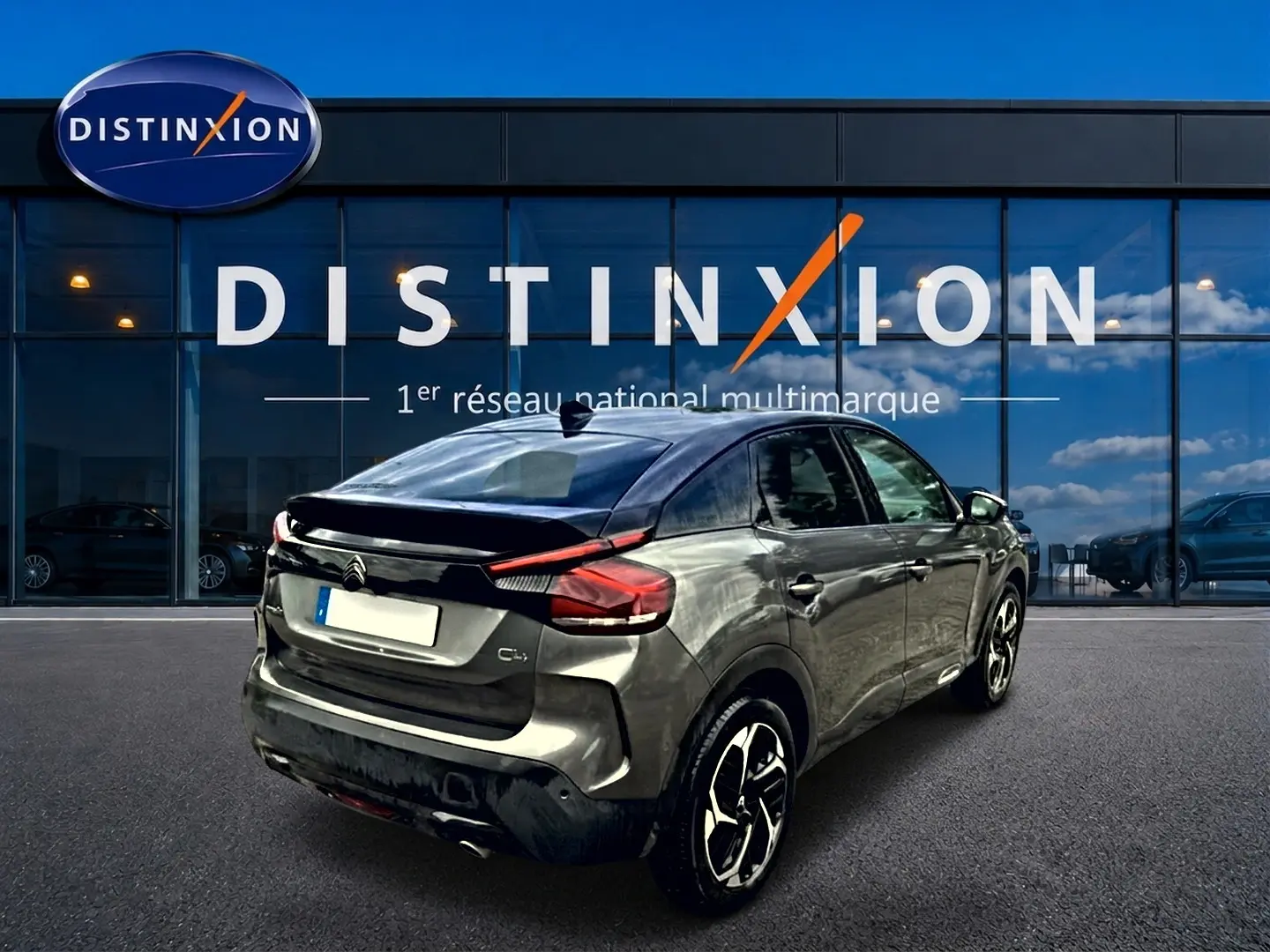 Vue 3/4 arrière droite d'une Citroën C4 gris métallisé avec jantes alu, garée devant une vitrine Distinxion.
