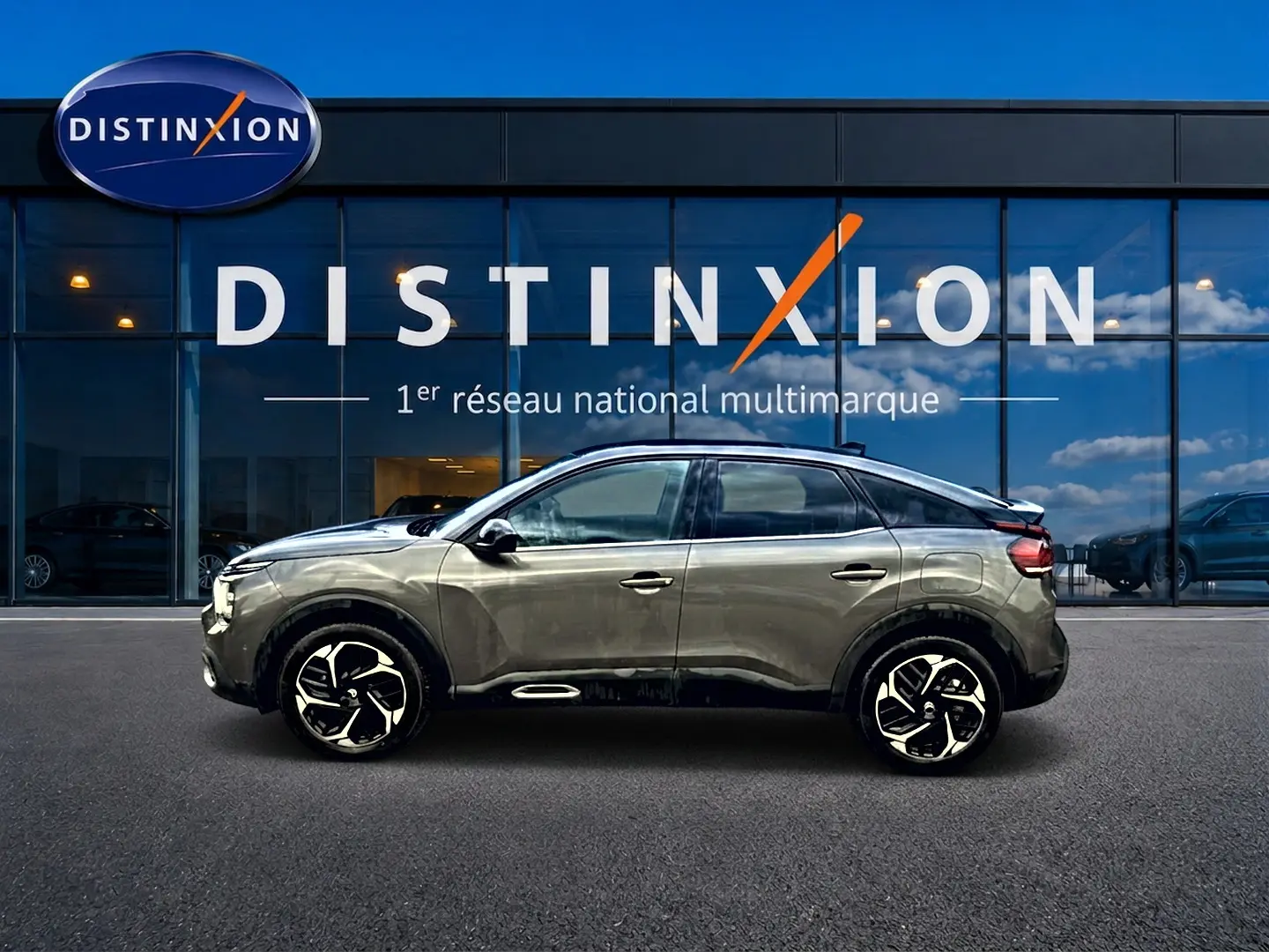 Profil côté gauche d'une Citroën C4 gris 2024 avec jantes alliage, devant une vitrine Distinxion.