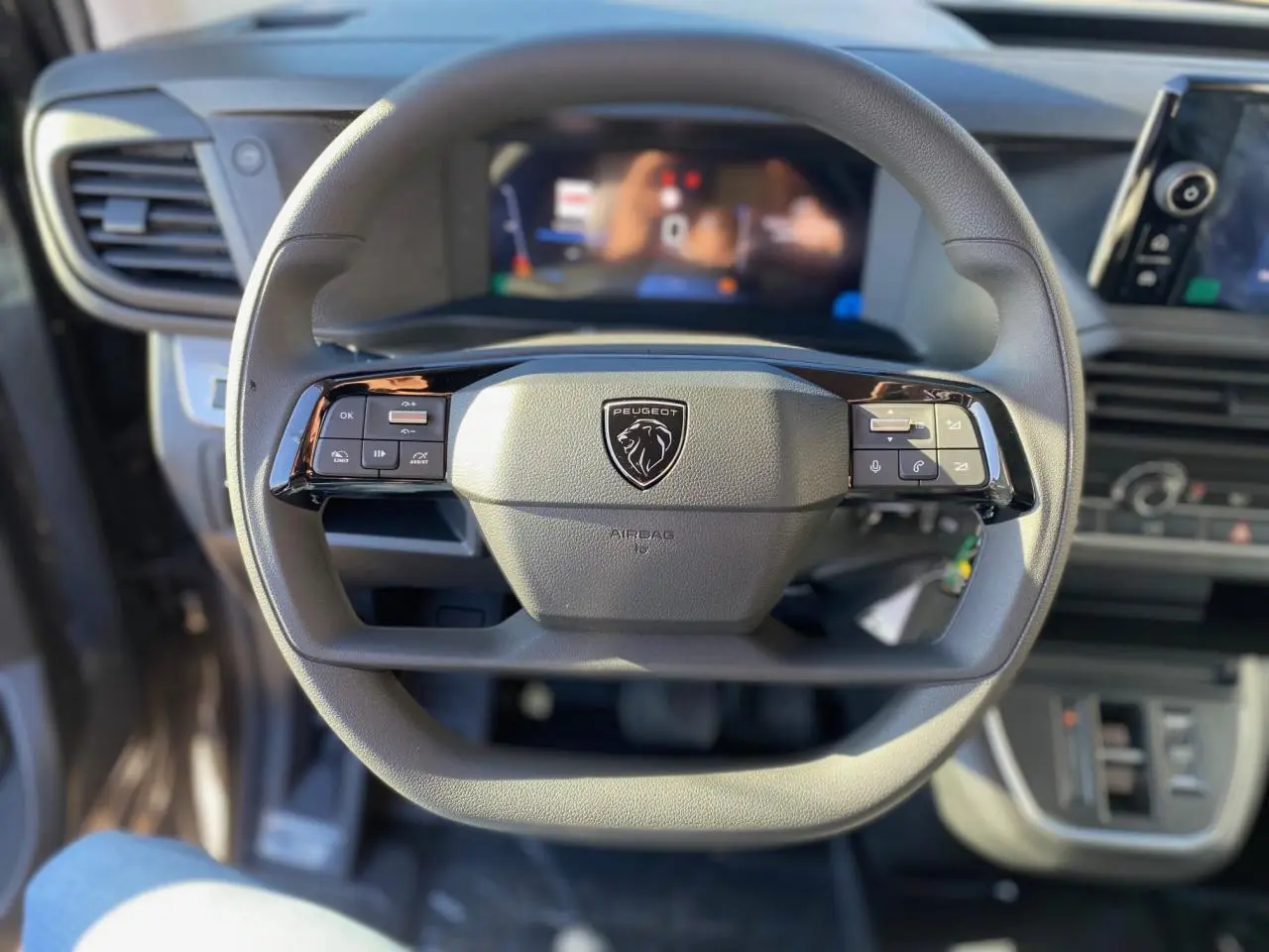 Vue rapprochée du volant multifonction gris du Peugeot Expert Fourgon 2026 avec tableau de bord numérique flou en arrière-plan.
