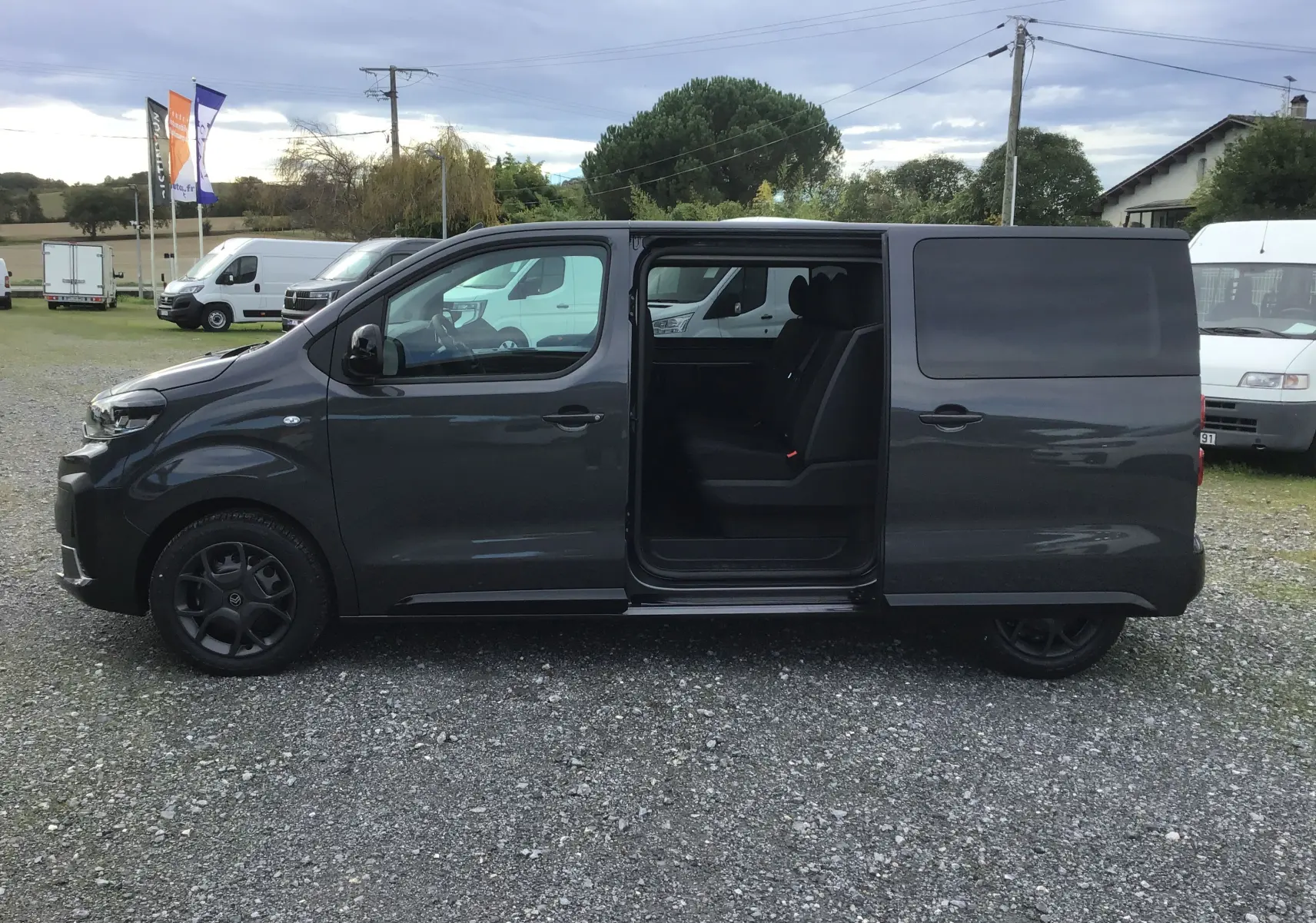 Vue latérale gauche d'un Citroën Jumpy gris titane avec porte coulissante ouverte révélant les sièges arrière noirs.