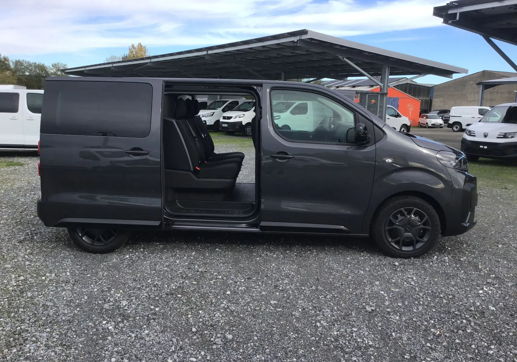 Vue latérale droite d'un Citroën Jumpy gris titane avec porte coulissante ouverte révélant les sièges passagers.