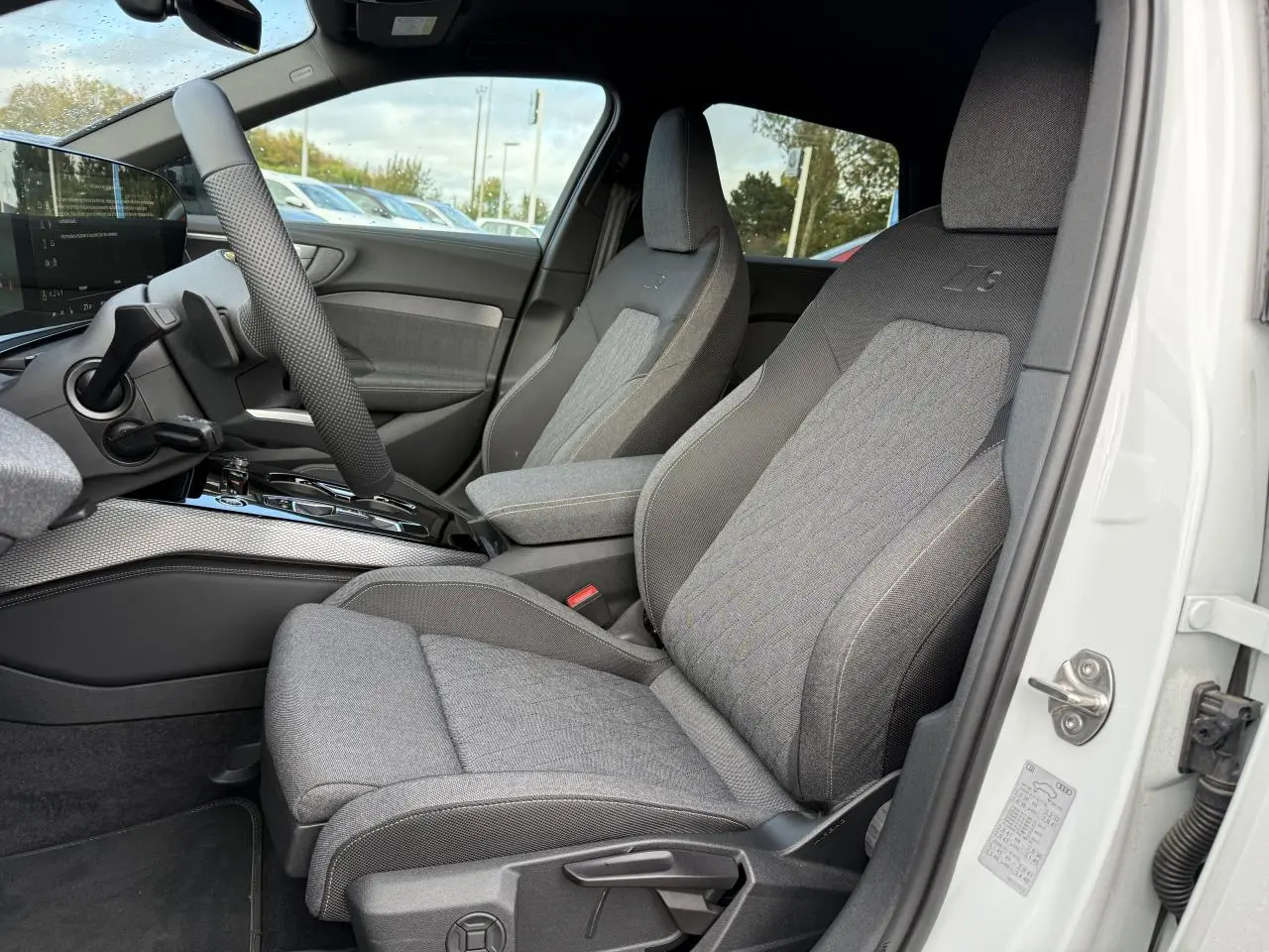 Vue intérieure côté conducteur de l'Audi A5 blanc glacier, sièges tissu gris avec logo S embossé sur appuie-tête.