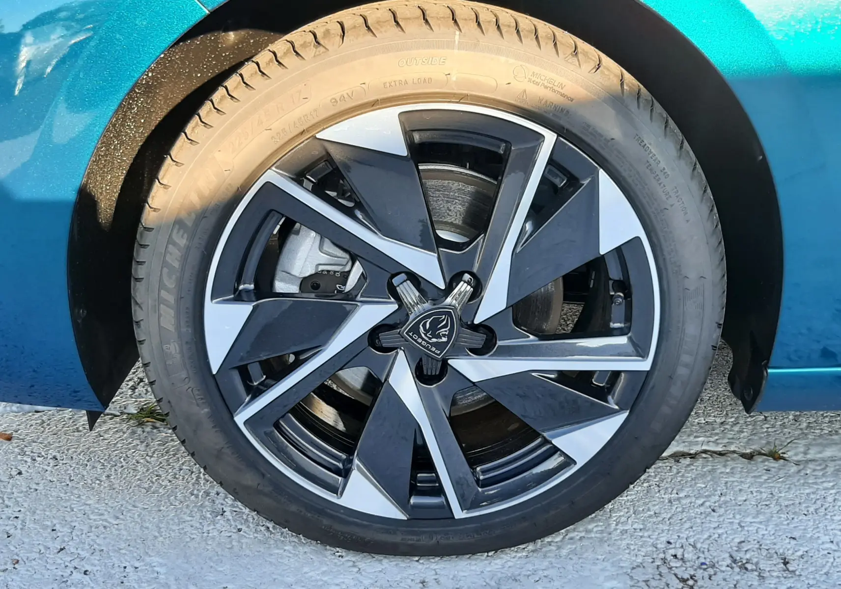 Gros plan sur la roue avant gauche d'une Peugeot 308 Bleu Obsession avec jante alliage bicolore moderne.