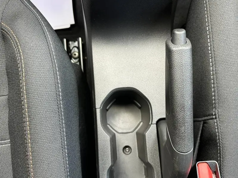 Vue plongeante sur le frein à main et porte-gobelets entre les sièges noirs du Dacia Sandero blanc Glacier 2025.