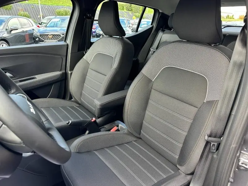 Intérieur de la Dacia Sandero 2025 vu côté conducteur, sièges tissu Expression noirs avec accoudoir central.
