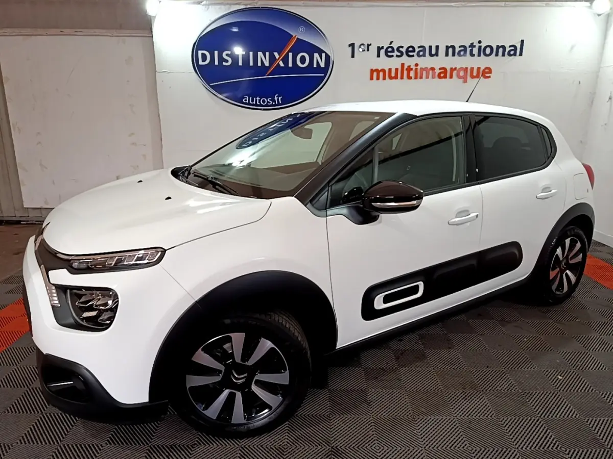 Citroën C3 blanche vue 3/4 avant droit, avec protections latérales noires et jantes bi-ton modernes.