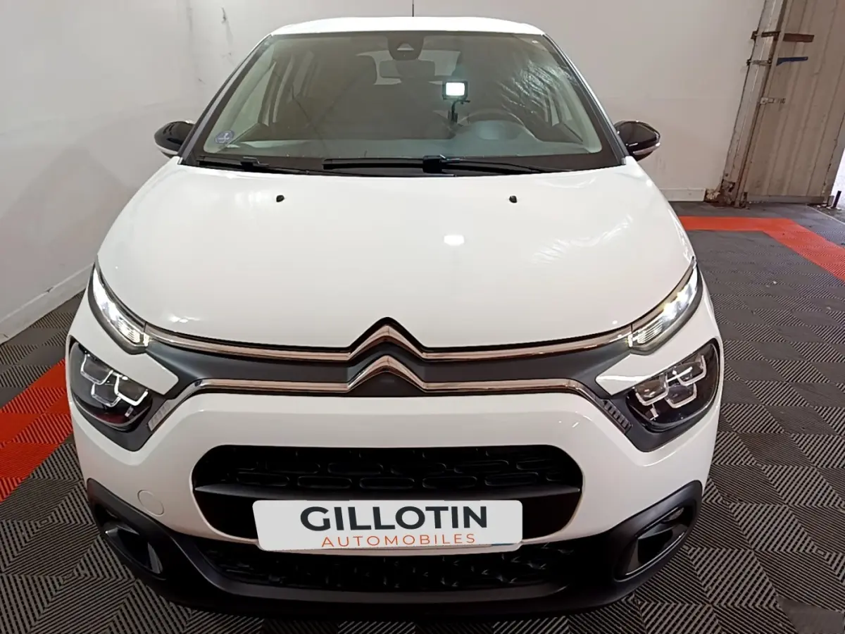 Vue frontale d'une Citroën C3 blanche 2023 avec phares LED et calandre noire distinctive en intérieur showroom.