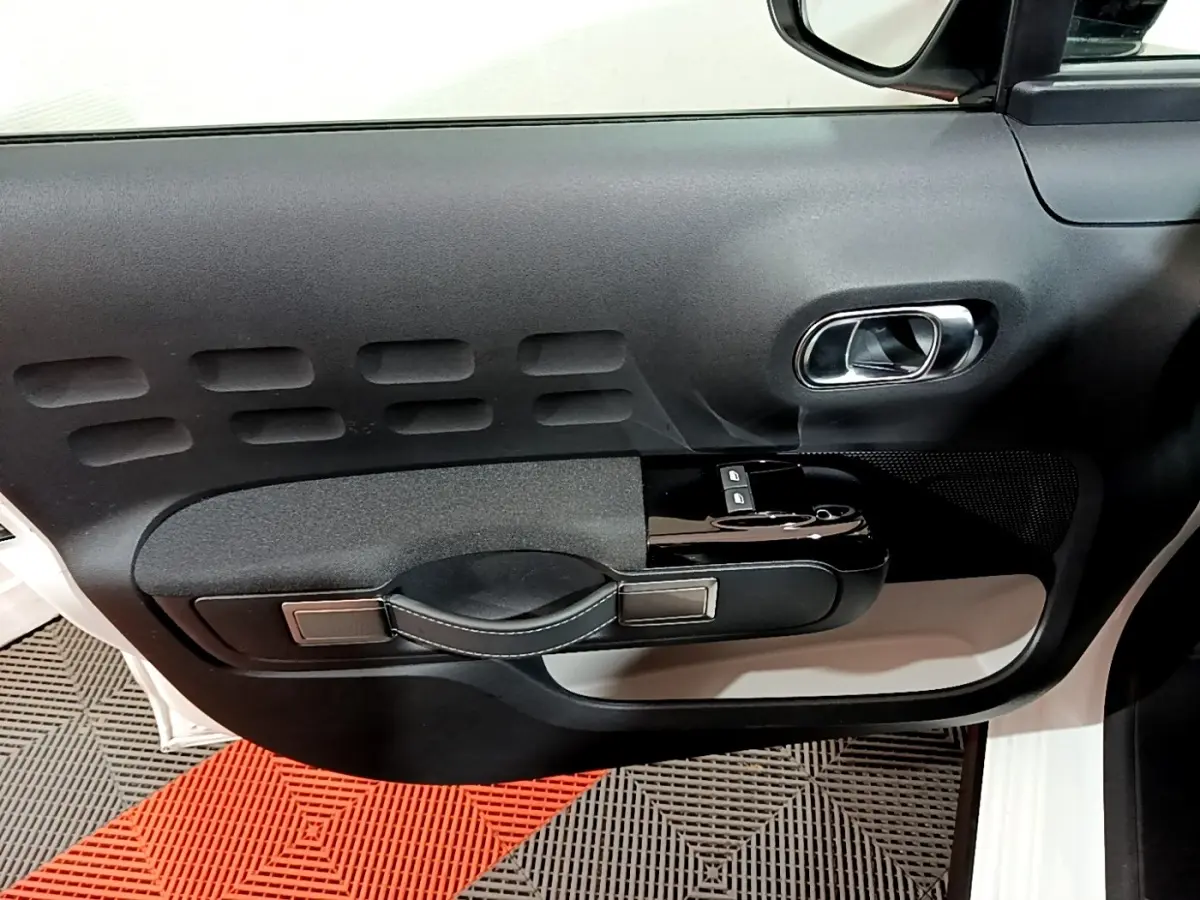 Vue intérieure côté gauche de la porte avant d'une Citroën C3 blanche avec poignée noire et commandes de vitres.