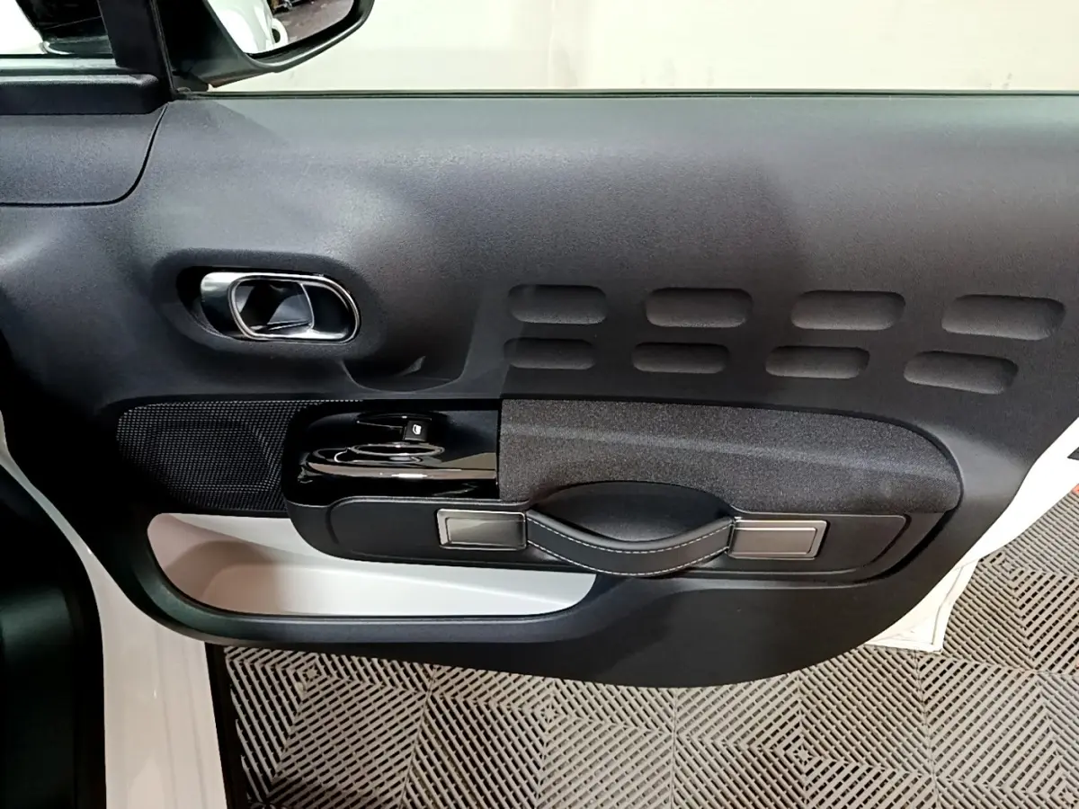 Détail de la porte côté conducteur noire et blanche de la Citroën C3 PureTech 83 Shine 2023 avec poignée et commandes intégrées.