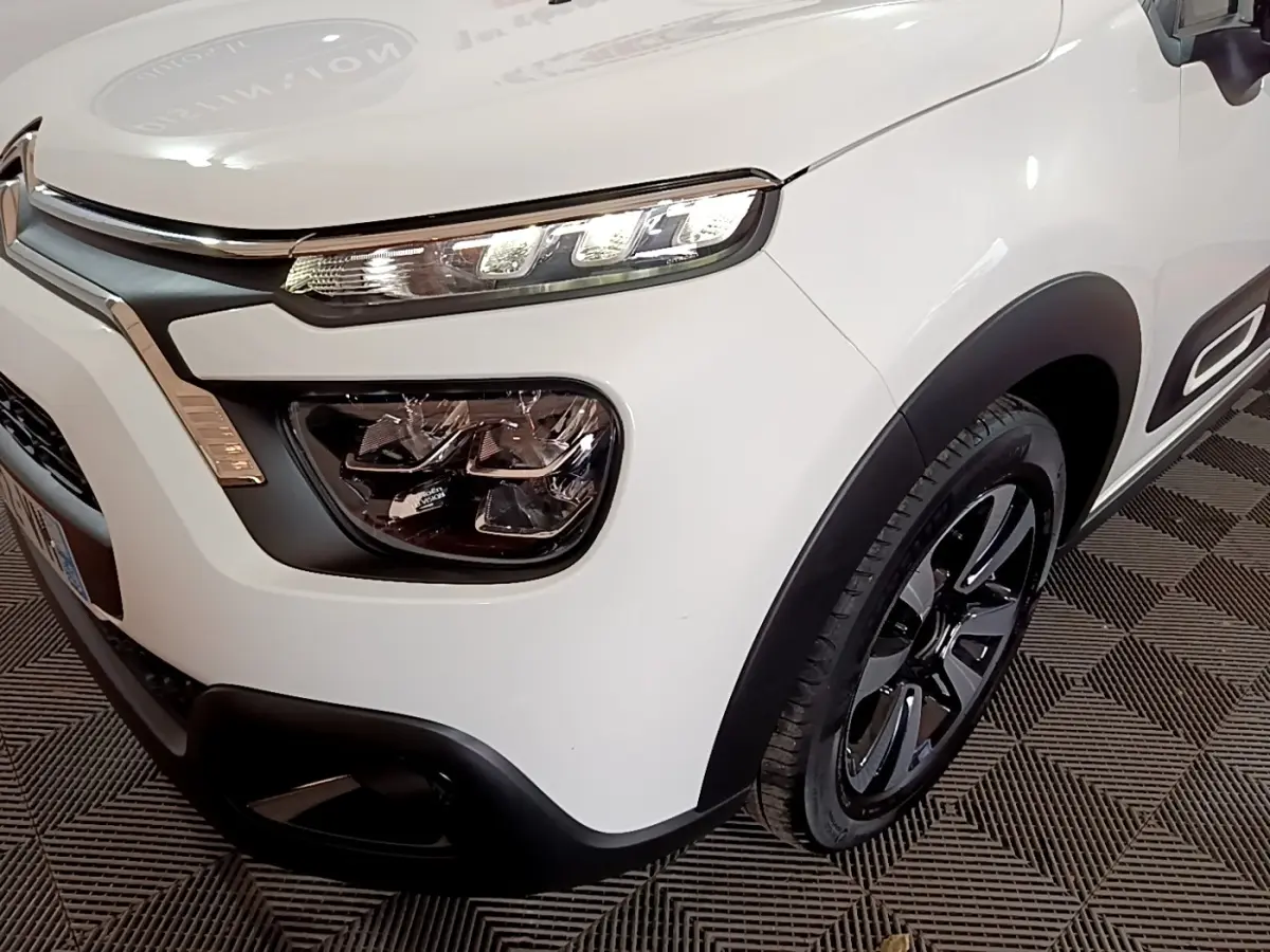 Vue 3/4 avant droit d'une Citroën C3 blanche 2023 avec phares LED et jantes noires distinctives.