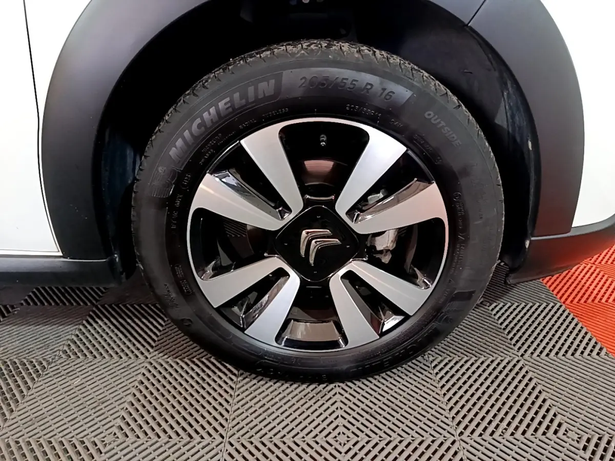 Gros plan sur la roue avant gauche d'une Citroën C3 blanche avec jante alliage bicolore et pneu Michelin.