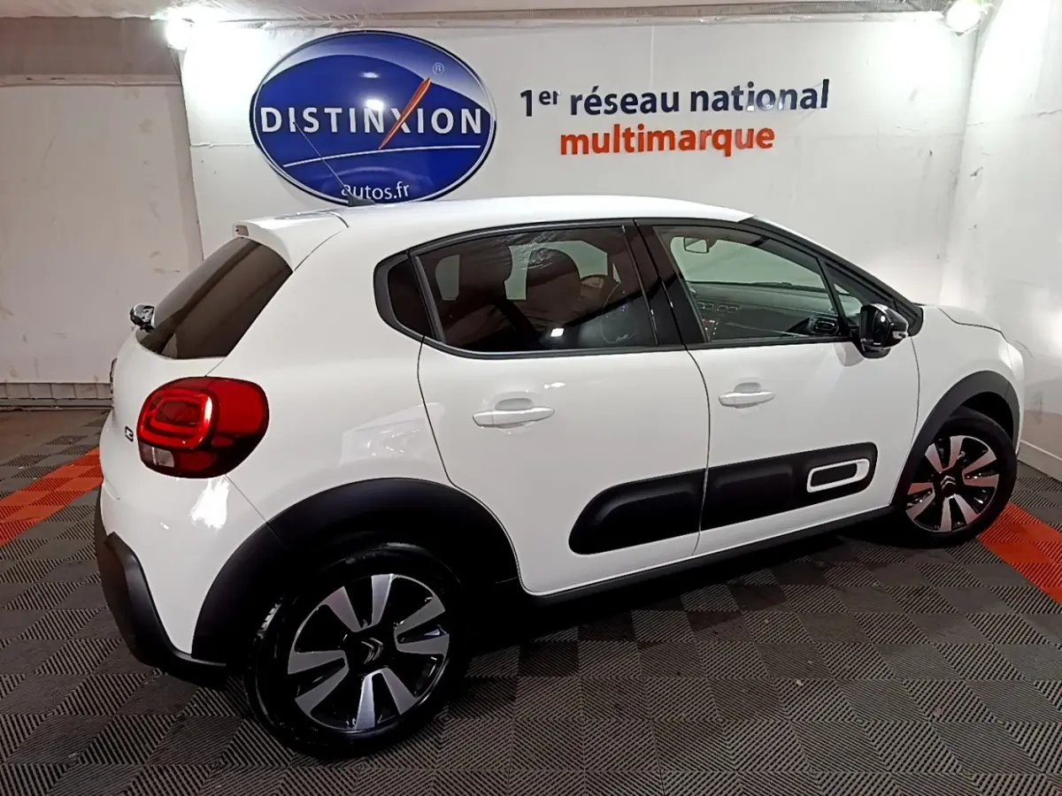 Profil côté droit d'une Citroën C3 blanche 2023 avec protections noires et jantes bicolores en intérieur showroom.