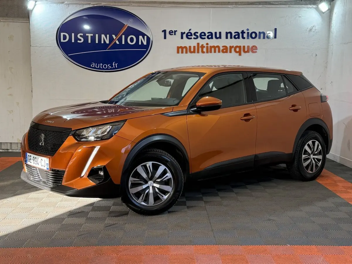 Peugeot 2008 orange vue 3/4 avant droit en intérieur, avec calandre noire et jantes bicolores.