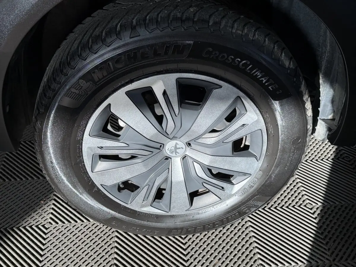 Gros plan sur la roue avant droite d’un Peugeot 2008 orange, avec jante argentée et pneu Michelin CrossClimate 2.