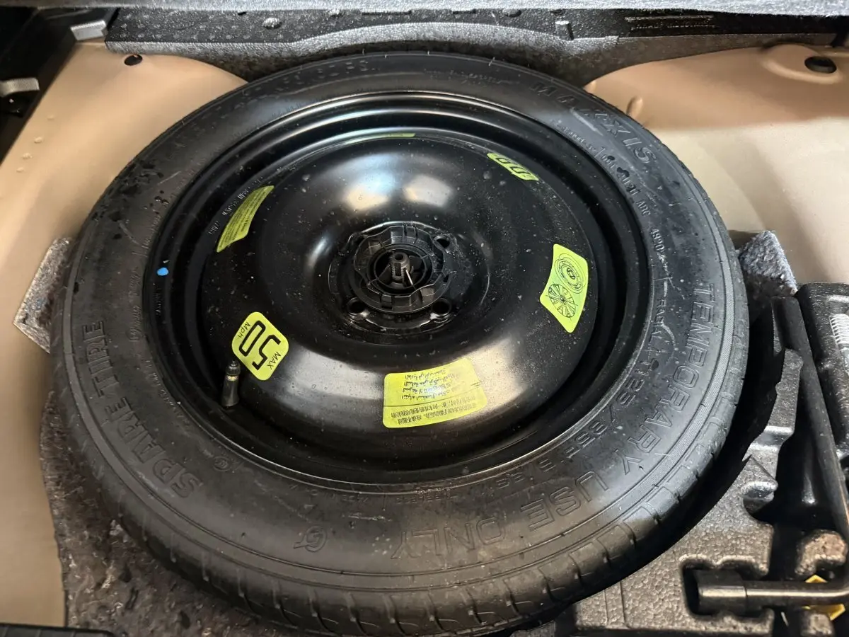 Gros plan sur la roue de secours noire dans le coffre d’une Peugeot 2008 orange, avec étiquettes jaunes visibles.