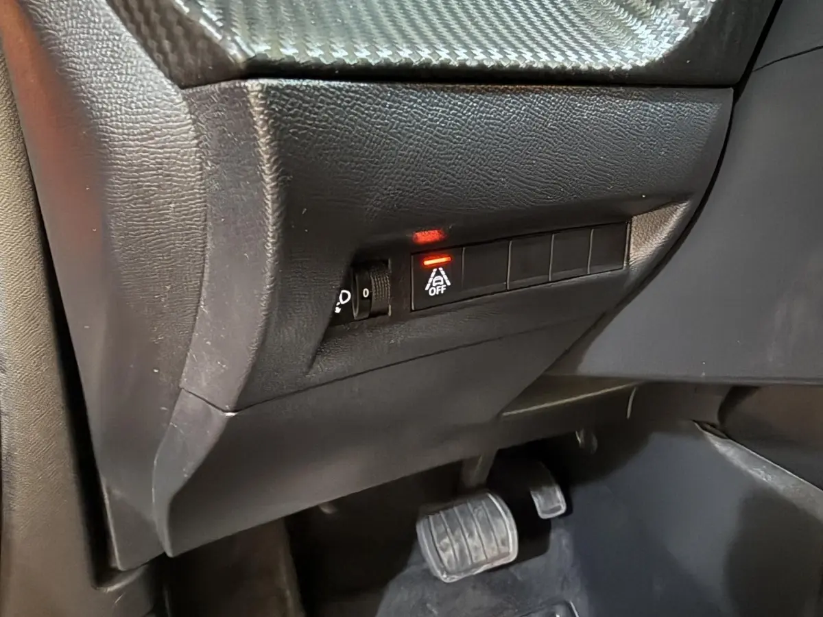 Vue intérieure côté conducteur du tableau de bord noir avec bouton d'arrêt de l'assistance à la conduite allumé dans un Peugeot 2008 orange.
