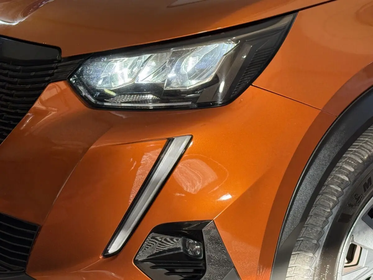 Gros plan sur le phare avant droit et la calandre d’un Peugeot 2008 orange métallisé avec antibrouillard intégré.