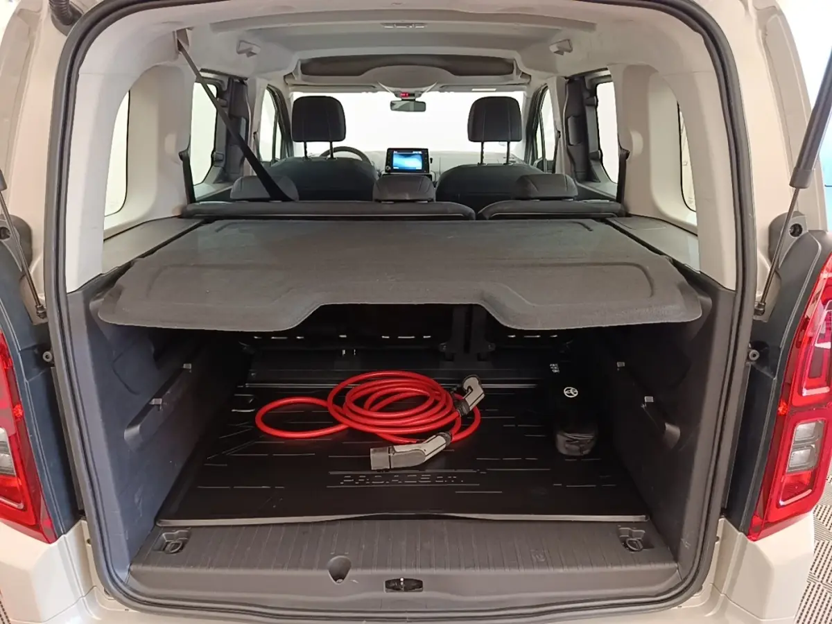 Vue arrière ouverte du Toyota Proace City Verso gris clair montrant le coffre avec câble de charge électrique rouge.