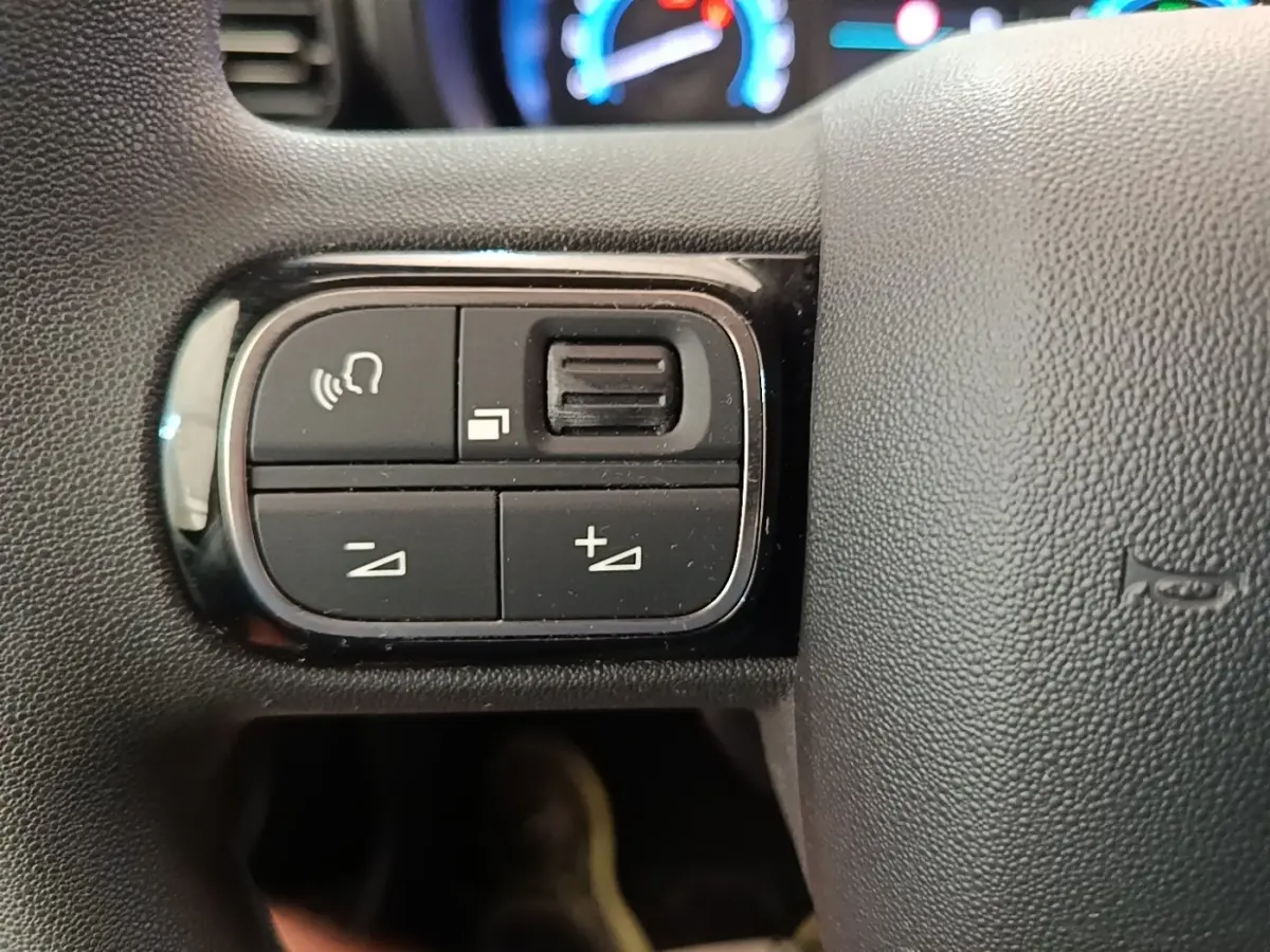 Gros plan sur les commandes gauche du volant noir du Toyota Proace City Verso électrique, avec tableau de bord flou en arrière-plan.