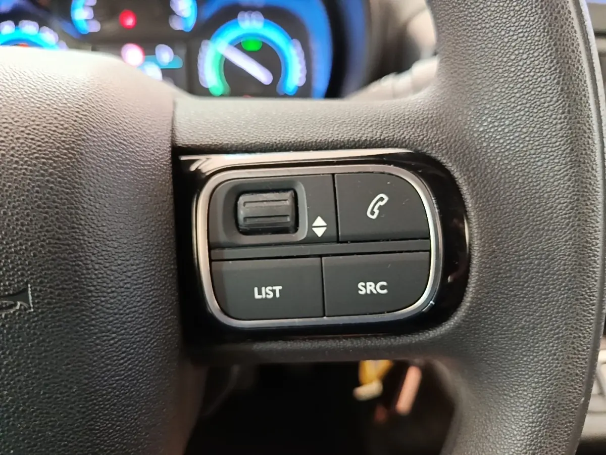 Gros plan sur les commandes gauche du volant noir du Toyota Proace City Verso électrique, avec tableau de bord lumineux en arrière-plan.