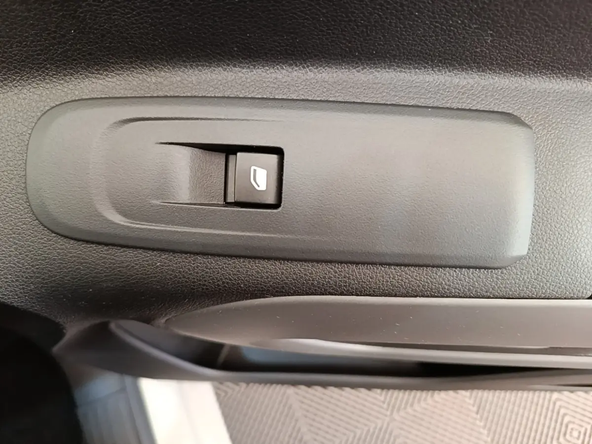 Gros plan sur le bouton de commande de lève-vitre intérieur noir dans une Toyota Proace City Verso gris clair.