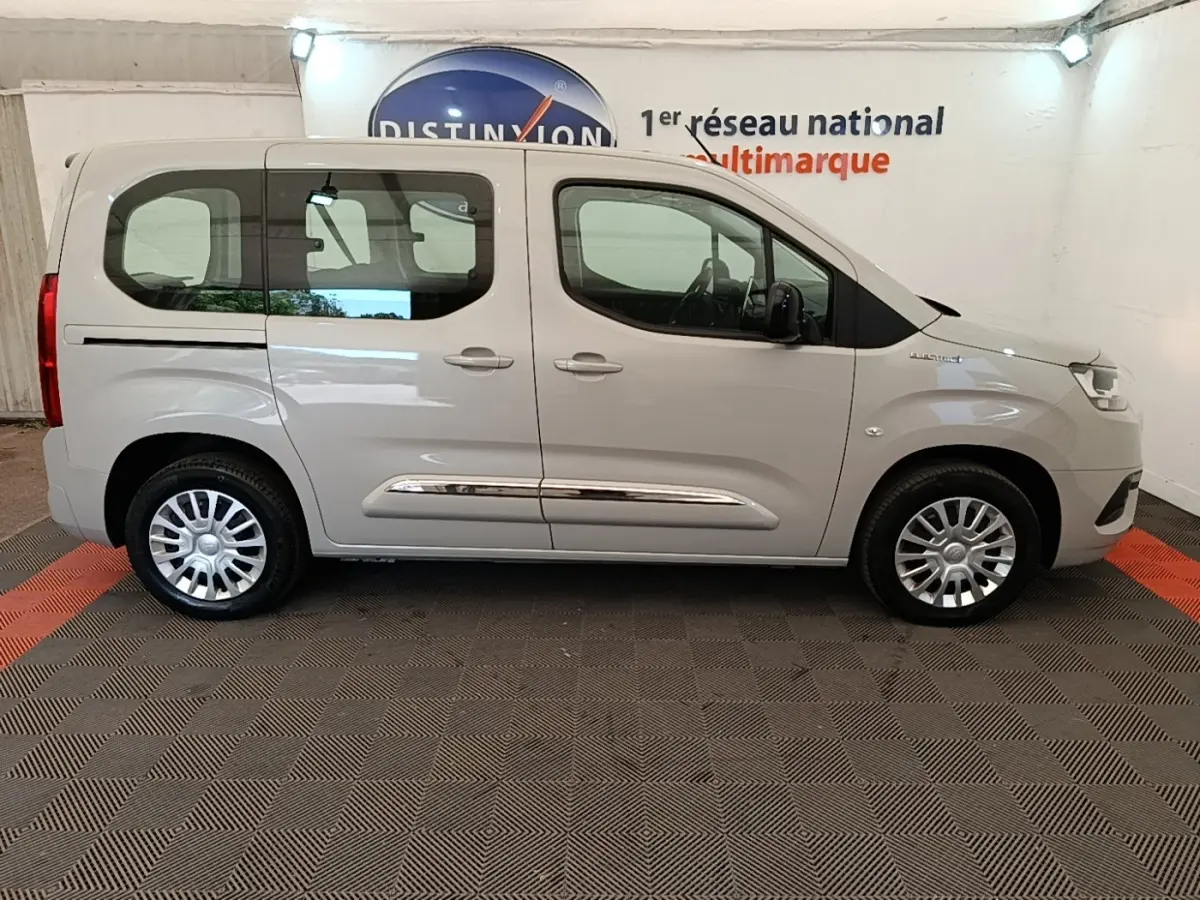 Vue de profil côté droit d'un Toyota Proace City Verso électrique gris clair avec jantes argentées en intérieur showroom.