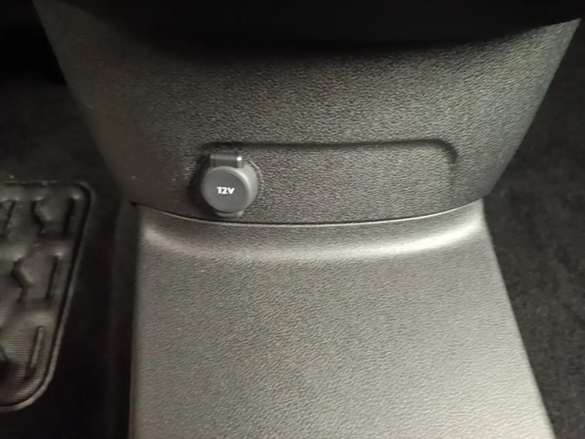 Prise 12V noire en gros plan sur la console centrale d’un Toyota Proace City Verso gris clair, vue intérieure basse.
