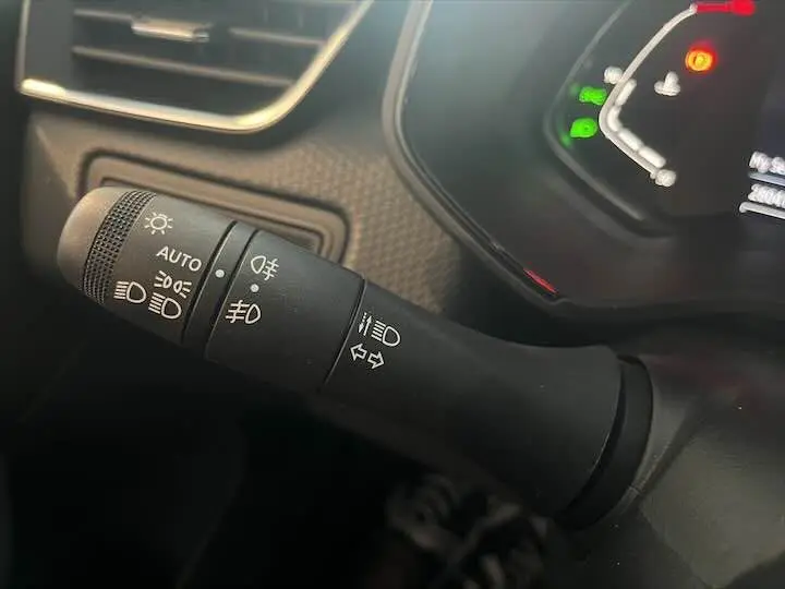 Gros plan sur la commande des phares et clignotants à gauche du tableau de bord d'une Renault Clio V blanche nacrée.