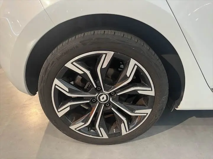 Gros plan sur la roue avant droite d'une Renault Clio V blanc nacré, jante alliage noire et argentée au design moderne.