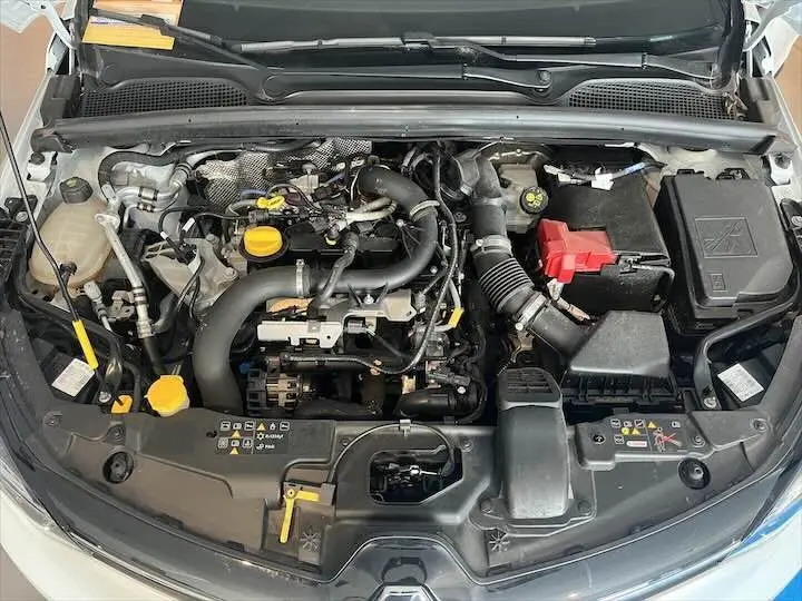 Vue plongeante sur le moteur essence d'une Renault Clio V blanc nacré, avec capot ouvert et détails mécaniques visibles.