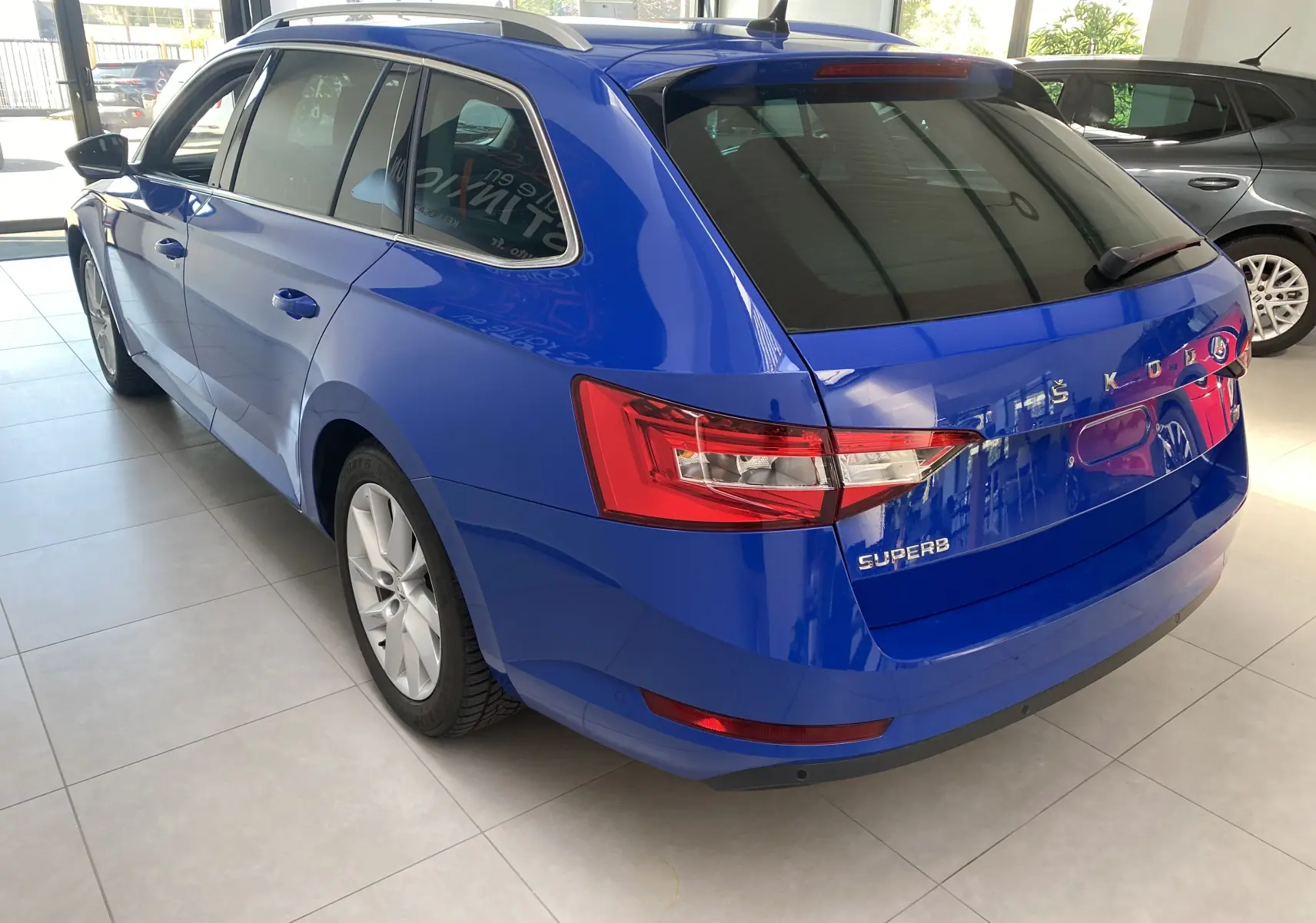 Vue 3/4 arrière gauche d'une Skoda Superb Combi bleu énergie, soulignant ses feux arrière et son design élégant.