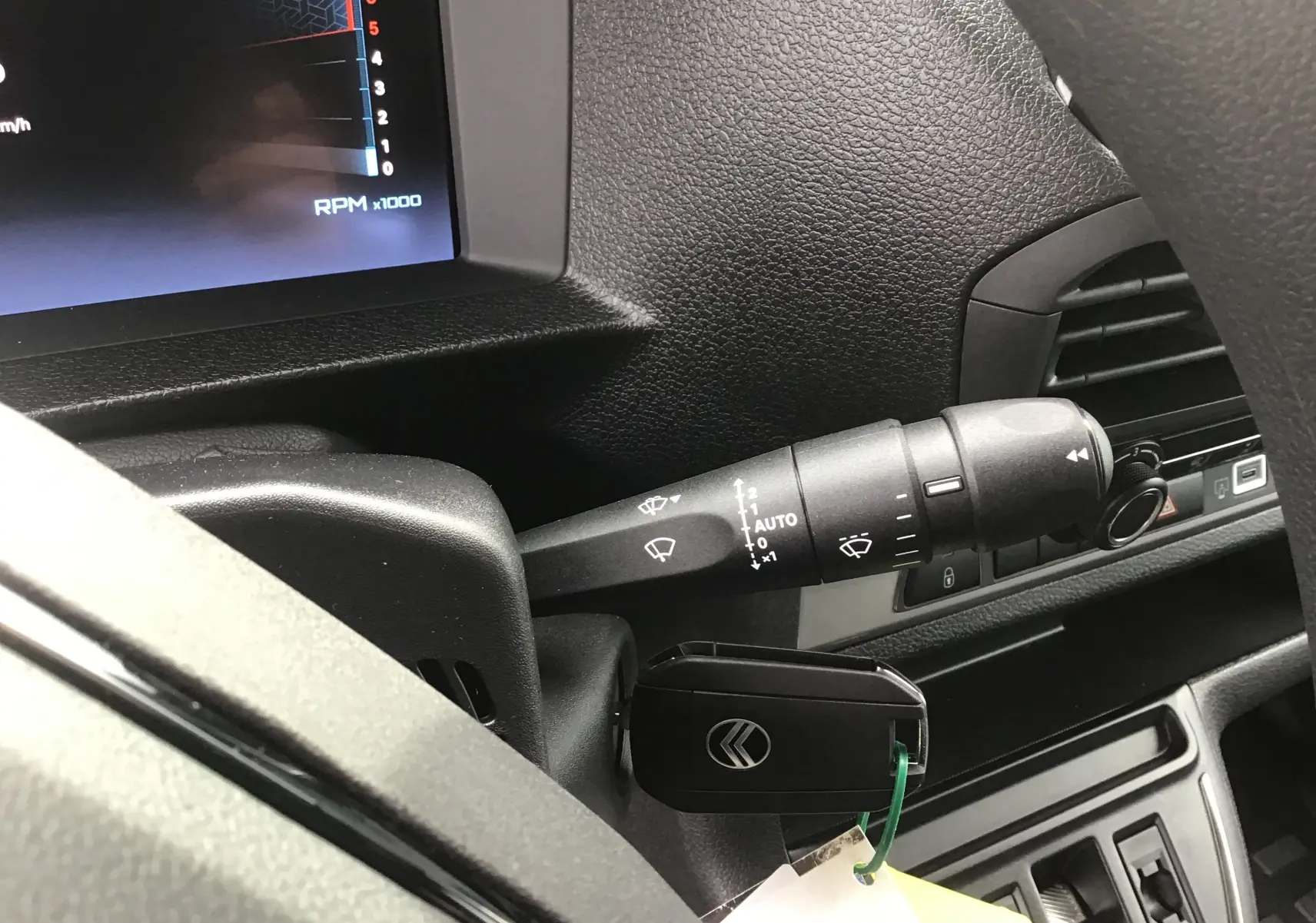 Gros plan sur la manette d'essuie-glace et la clé de contact dans le tableau de bord noir du Citroën Jumpy cabine approfondie blanc.
