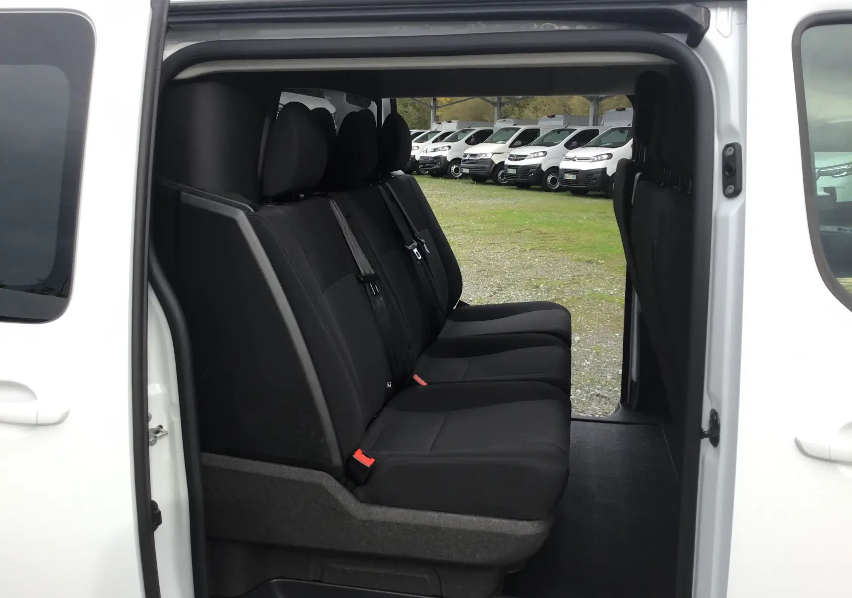 Vue latérale intérieure des sièges noirs du Citroën Jumpy Cabine Approfondie blanc avec porte coulissante ouverte.