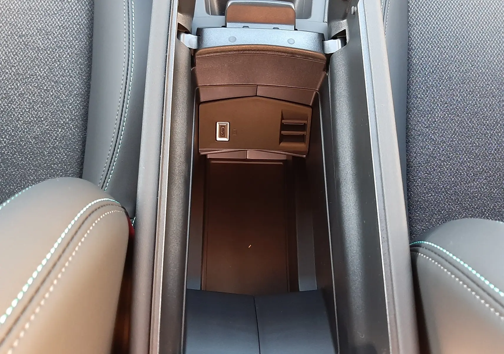 Vue plongeante sur le rangement central ouvert entre les sièges noirs avec surpiqûres bleues d'une Peugeot 308 2025.