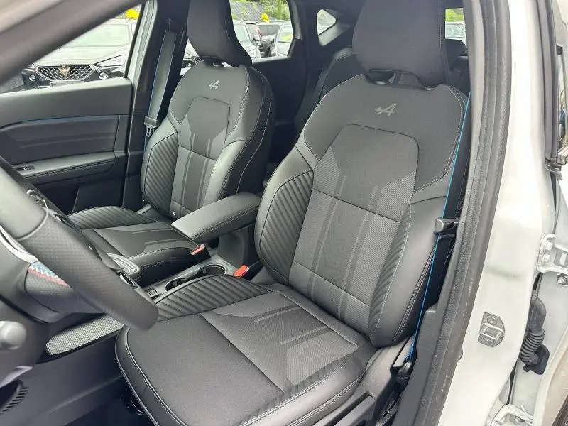 Intérieur du Renault Captur 2025 hybride, vue côté gauche sur sièges noirs avec logo Alpine brodé et surpiqûres bleues.