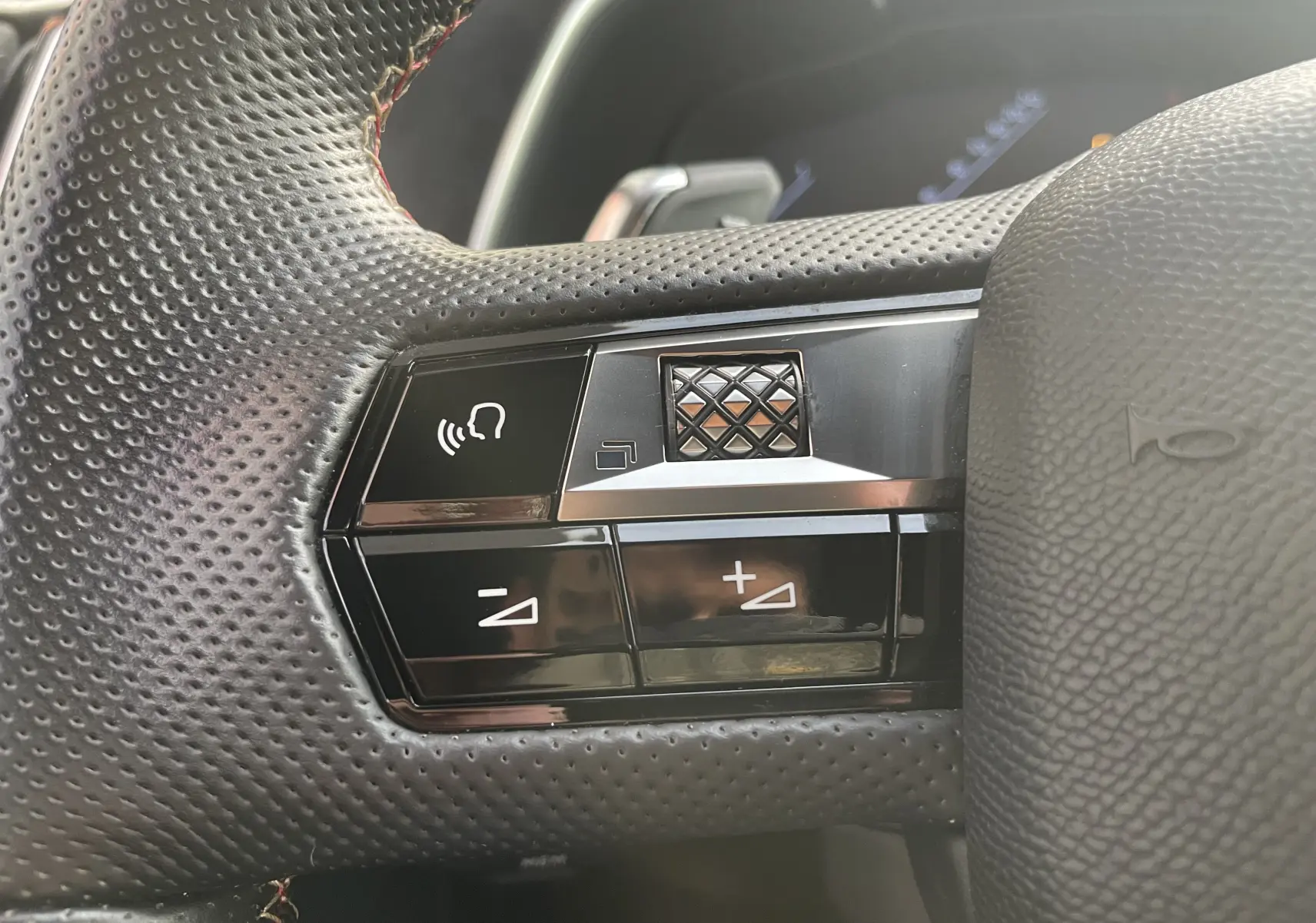 Gros plan sur les commandes du volant perforé noir du DS7 gris, avec boutons de volume et commande vocale.