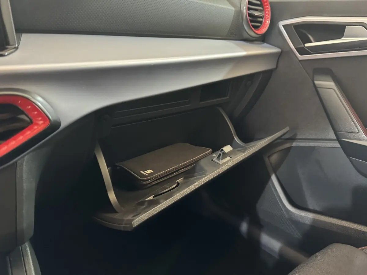 Gros plan sur la boîte à gants ouverte côté passager de la SEAT IBIZA 1.0 TSI 110 FR 2024 avec intérieur noir et accents rouges.