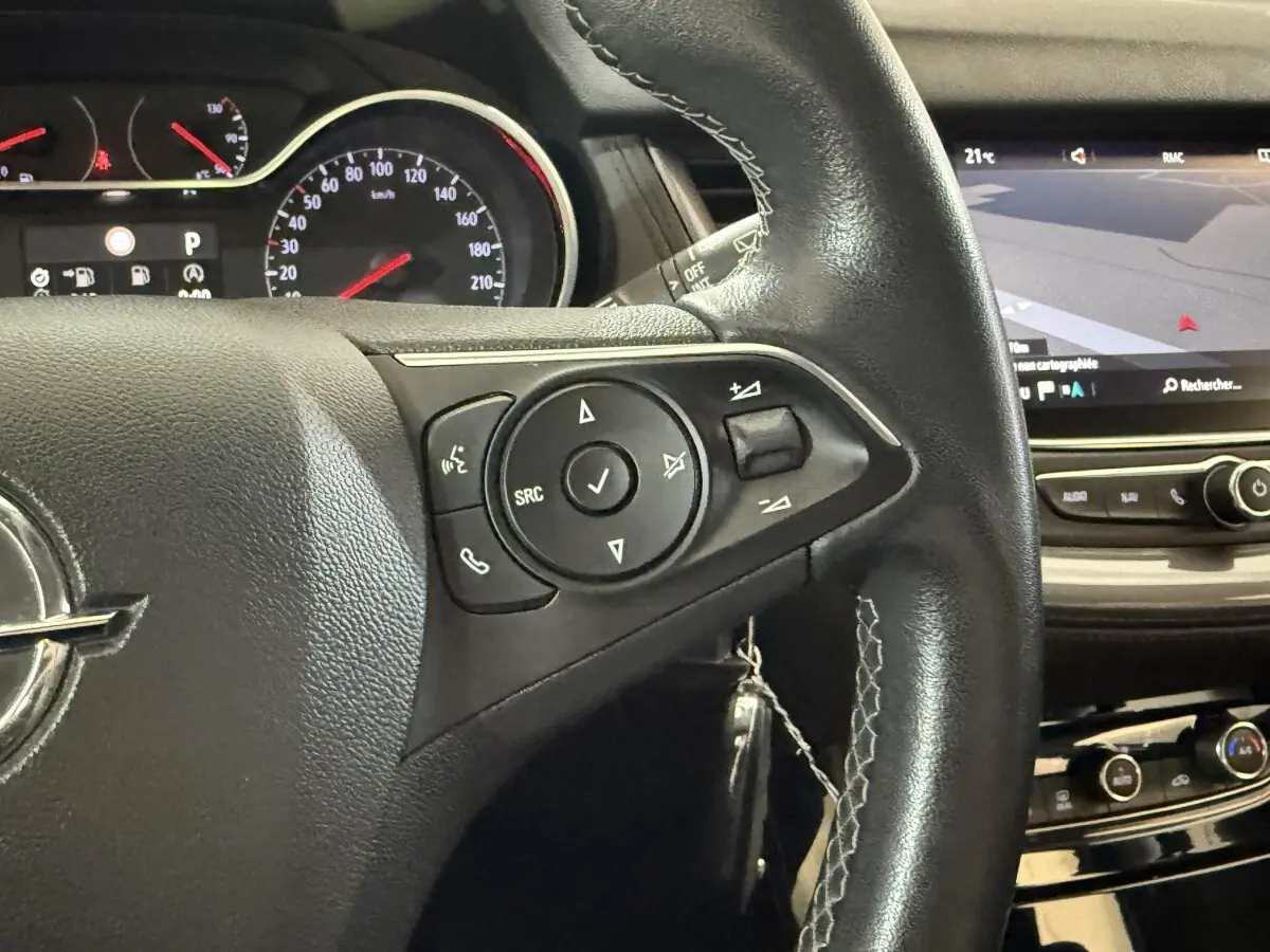 Gros plan sur le volant cuir noir de l’Opel Grandland X 2021 avec commandes multifonctions et écran tactile en arrière-plan.